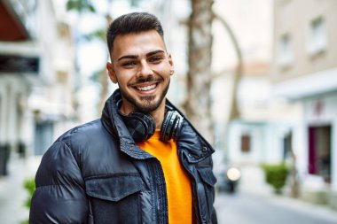 Sakallı yakışıklı, neşeli ve kendine güvenen, kışlık palto ve kulaklık takan bir İspanyol.