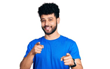 Sıradan mavi tişörtlü, sakallı genç Arap adam mutlu ve komik yüzüyle kamerayı işaret ediyor. iyi enerji ve titreşimler. 