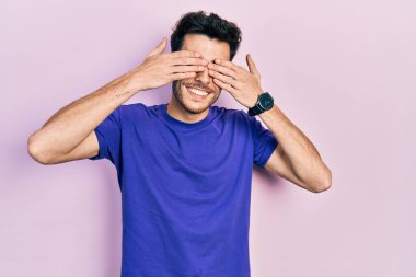 Gündelik tişört giyen, elleri gülücüklü, neşeli gözlerle gözlerini kapayan İspanyol genç bir adam. kör kavram. 