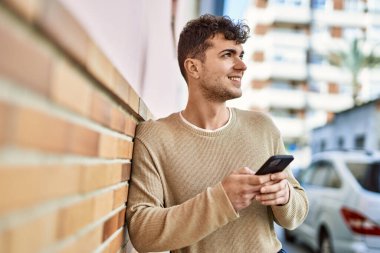 Genç İspanyol adam şehirde akıllı telefon kullanarak mutlu gülümsüyor.