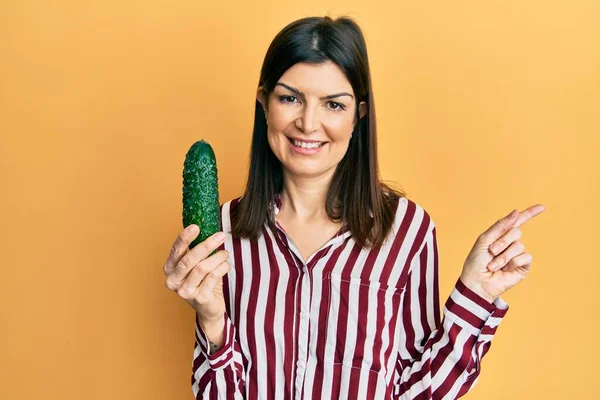 Junge Hispanische Frau Hält Gurke Lächelnd Glücklich Und Zeigt Mit — Stockfoto