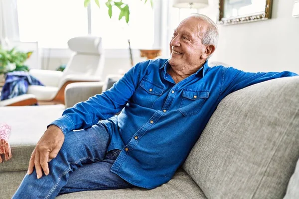 灰色の髪のシニアは 彼の家のリビングルームのソファに座っています Mature Man Smiling Happy Home — ストック写真