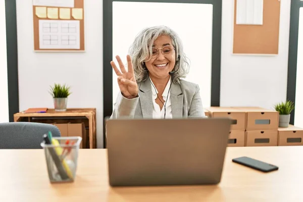 中年女商人坐在写字台上 在办公室里用笔记本电脑办公 用手指指指第三号 面带微笑 自信而快乐 — 图库照片