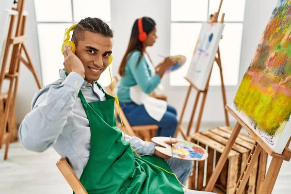 Young latin painter couple smiling happy painting and using headphones at art studio