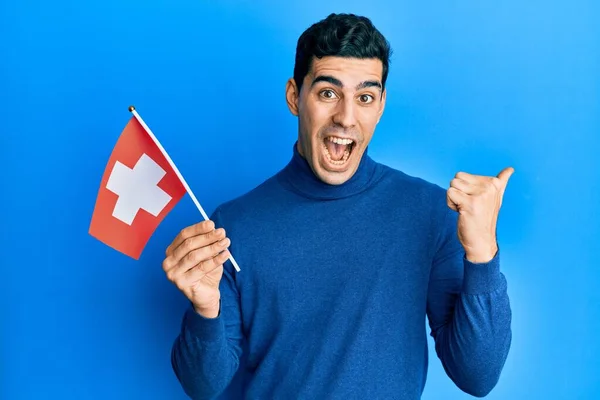 Bonito Hispânico Segurando Bandeira Suíça Apontando Polegar Para Lado Sorrindo — Fotografia de Stock