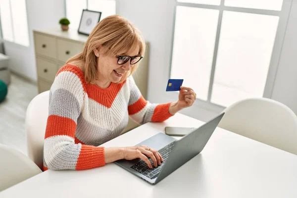 中年金发女人在家用笔记本电脑和信用卡购物 — 图库照片