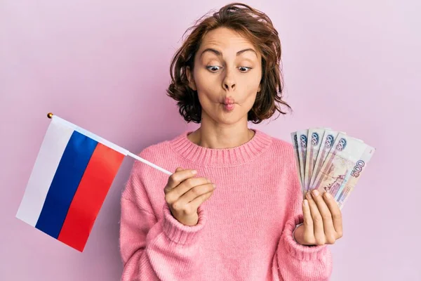 年轻的黑发女子举着俄罗斯国旗和卢布钞票 用嘴和眼神做鱼脸 疯狂而滑稽 — 图库照片