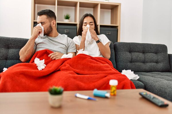 Young latin ill couple using napkin sititng on the sofa at home.