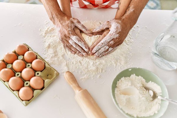 Hands of couple kneading dough at kitchen.