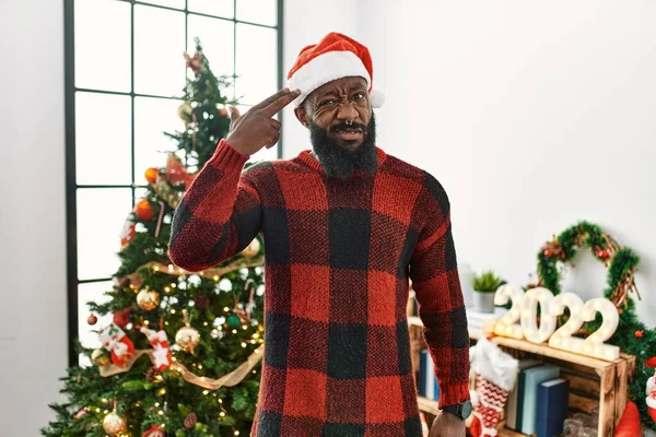 サンタの帽子をかぶったアフリカ系アメリカ人の男がクリスマスツリーで立って銃のように頭に手や指を指して自分自身を殺す 自殺のジェスチャー — ストック写真
