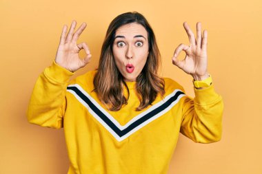Gündelik kıyafetler giyen genç İspanyol kız şaşırmış ve şok olmuş görünüyor. Tamam sembolünü parmaklarıyla yapıyor. çılgın ifade 