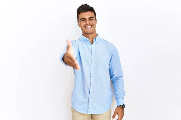 ビジネスシャツを着た若いヒスパニック系の男性が孤立した背景の上に立ち 挨拶や歓迎として握手を提供して笑顔 成功したビジネス — ストック写真
