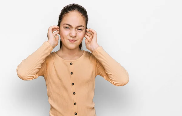 美しいブルネットの女の子は 大きな音楽のノイズのためにいらいらした表情で指で耳を覆うカジュアルなセーターを着ています 聴覚障害の概念 — ストック写真