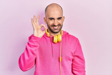 Spor kıyafetleri giyen, kulaklık takan, gülümseyen genç kel adam el ve parmaklarıyla 