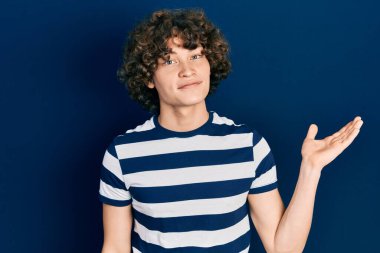 Yakışıklı, çizgili tişört giyen neşeli bir şekilde gülümseyen ve avuç içi kameraya bakan genç bir adam.. 