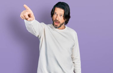 Orta yaşlı, günlük giysiler giyen beyaz bir adam parmağıyla işaret ederek şaşırmış, ağzı açık, şaşırmış, ön tarafta bir şey var. 