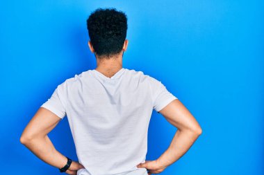 Beyaz tişörtlü, sakallı genç Arap adam kolları vücudunda geriye doğru bakıyor. 