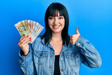 Genç İspanyol kadın elinde Peru sol banknotları tutarken mutlu ve olumlu gülümsüyor, başparmağıyla mükemmel ve onay işareti yapıyor. 