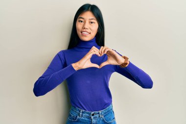 Gündelik kıyafetler giyen, aşık gülümseyen, elleriyle kalp sembolü yapan genç Çinli bir kadın. romantik kavram. 