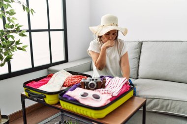 Güzel, orta yaşlı İspanyol bir kadın valizine yazlık giysiler yerleştiriyor kendini iyi hissetmiyor ve soğuk algınlığı veya bronşitin belirtisi olarak öksürüyor. sağlık hizmeti kavramı. 