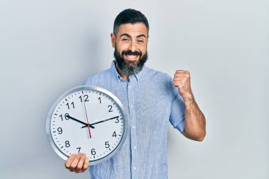 Latin asıllı genç adam büyük bir saat tutuyor gururla bağırıyor, zaferi kutluyor ve başarıyı kollarını kaldırarak kutluyor. 