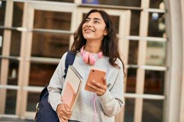 Genç ortadoğulu kız şehirde akıllı telefon kullanarak mutlu bir şekilde gülümsüyor..
