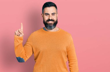 Sakallı, sıradan bir kazak giyen İspanyol bir numaralı parmağını gösterip gülümseyerek mutlu ve kendine güvenen bir adam.. 