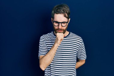 Sakallı, çizgili tişörtlü ve gözlüklü beyaz bir adam kendini iyi hissetmiyor ve soğuk algınlığı veya bronşitin belirtisi olarak öksürüyor. sağlık hizmeti kavramı. 