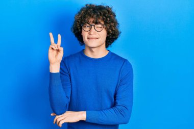 Yakışıklı, sıradan kıyafetler giyen ve gözlüklü, gülümseyen, kameraya göz kırpan, zafer işareti yapan genç bir adam. İki numara.. 