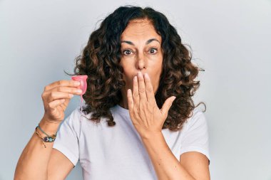 Orta yaşlı İspanyol bir kadın, elinde regl fincanı tutarak ağzını eliyle kapatıyor, şok geçiriyor ve hata yapmaktan korkuyor. şaşırmış ifade 