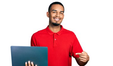 Genç Afro-Amerikalı bir adam bilgisayarla çalışıyor. Elle ve parmakla işaret ederek mutlu bir şekilde gülümsüyor. 