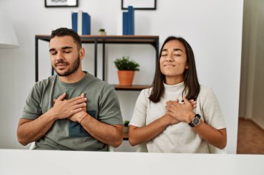 Masada oturan, elleri göğsünde, gözleri kapalı ve yüzlerinde minnet dolu jestlerle gülümseyen Latin bir çift. sağlık kavramı. 