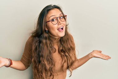 Sıradan kıyafetler giyen, gözlüklü, kafası karışık, elleri ve kolları havada genç İspanyol bir kız. şüphe kavramı. 