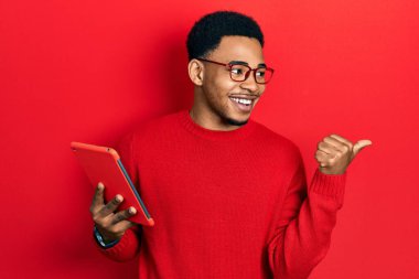 Genç Afro-Amerikan adam dokunmatik bir cihaz kullanıyor. Parmağını yana doğru uzatıyor. Ağzını açıp gülümsüyor. 