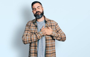 Sakallı, sıradan tişörtlü, göğsünde elleri kapalı, yüzünde minnet ifadesi olan İspanyol bir adam. sağlık kavramı. 