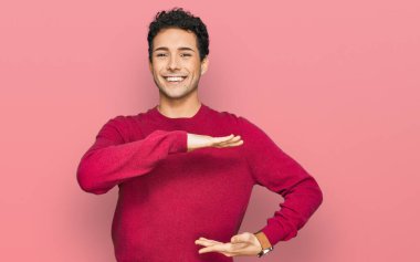 Elleriyle el kol hareketi yapan, büyük ve büyük beden işareti gösteren sıradan kıyafetler giyen genç yakışıklı bir adam. Kameraya bakıp gülümsüyor. ölçüm kavramı. 