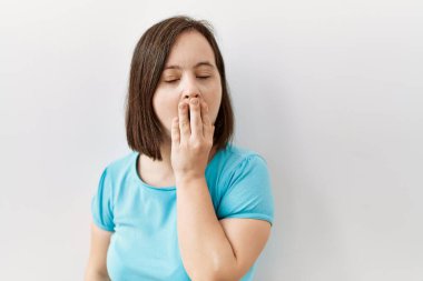 Genç Down sendromlu kadın izole arka planda dikiliyor. Elle ağzını kapatmaktan sıkılmış. Huzursuz ve uykulu.. 