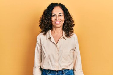 Orta yaşlı İspanyol kadın mutlu ve havalı bir gülüşü olan sıradan kıyafetler giyiyor. şanslı kişi. 