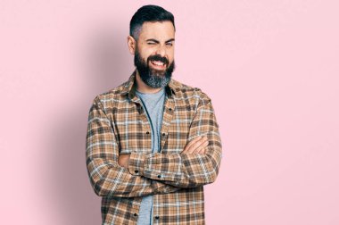 Kollarını kavuşturmuş sakallı İspanyol bir adam kameraya seksi bir ifadeyle bakıyor, neşeli ve mutlu bir yüzle.. 