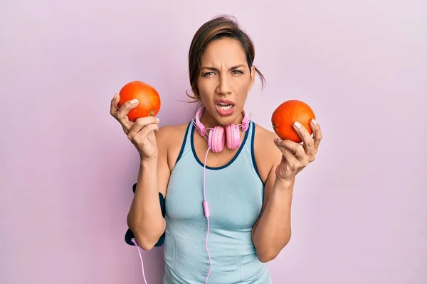 Mujer Latina Joven Usando Ropa Gimnasio Usando Auriculares Sosteniendo Naranjas —  Fotos de Stock