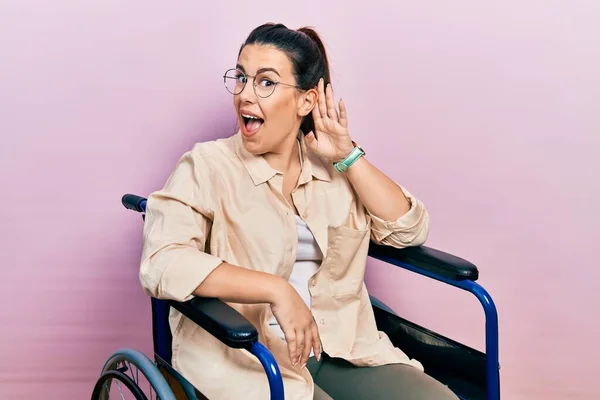 若いヒスパニック系の女性の車椅子に手を耳に噂やゴシップに耳を傾け笑みを浮かべて座っている 聴覚障害の概念 — ストック写真