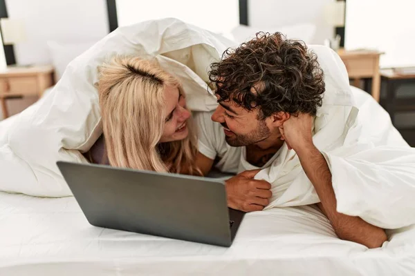 年轻漂亮的夫妇在床上看着铺满床单的电影 — 图库照片
