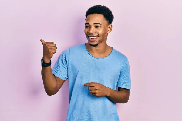 身穿休闲蓝T恤的年轻的非洲裔美国人面带微笑 面带微笑 并竖起大拇指指向旁边 — 图库照片