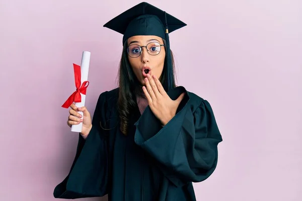 Mladá Hispánka Maturitní Uniformě Držící Diplom Zakrývající Ústa Rukou Šokovaná — Stock fotografie