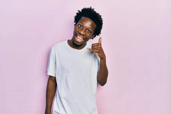 若いアフリカ系アメリカ人の男性は カジュアルな白いTシャツを着て 電話で話すような手や指で電話のジェスチャーをして笑っています コミュニケーションの概念 — ストック写真