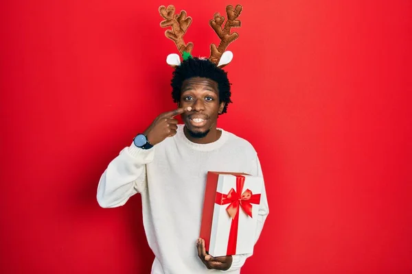 Jovem Afro Americano Vestindo Chapéu Natal Veado Segurando Presente Apontando — Fotografia de Stock