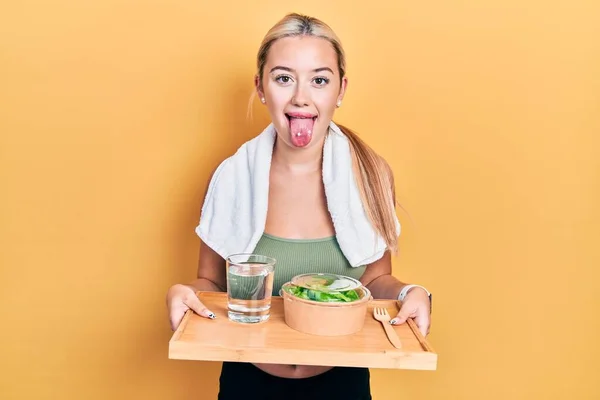穿着运动服的金发小女孩吃着健康的食物 伸出舌头 高兴得笑出声来 — 图库照片