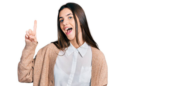 Юная брюнетка-подросток в обычной белой рубашке и куртке показывает пальцем вверх с успешной идеей. Взволнован и счастлив. номер один. 