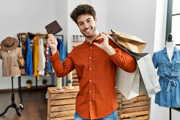 若いヒスパニック系の顧客の男笑顔幸せな保持ショッピングバッグと革財布で衣料品店 — ストック写真