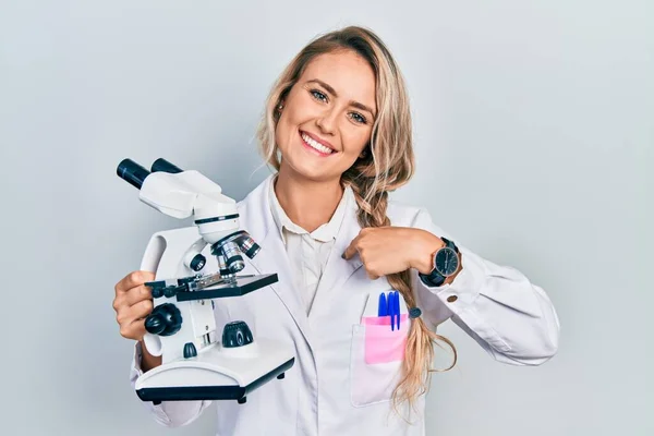 Hermosa Joven Rubia Sosteniendo Microscopio Señalando Dedo Uno Mismo Sonriendo —  Fotos de Stock